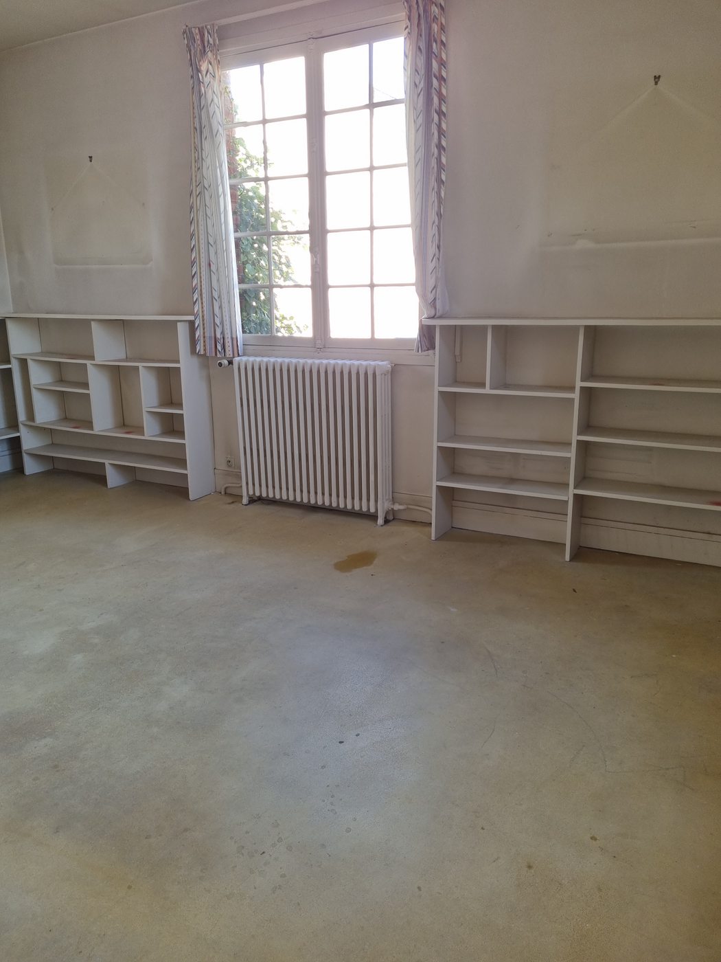 Radiateur fonte remplacé entre deux bibliothèques sous une fenêtre