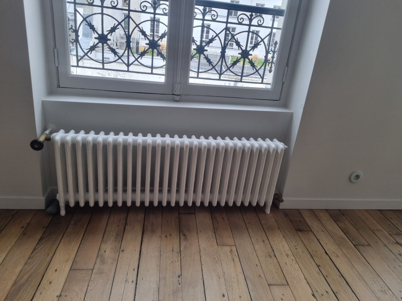 Radiateur posé sous une fenêtre dans un appartement parisien
