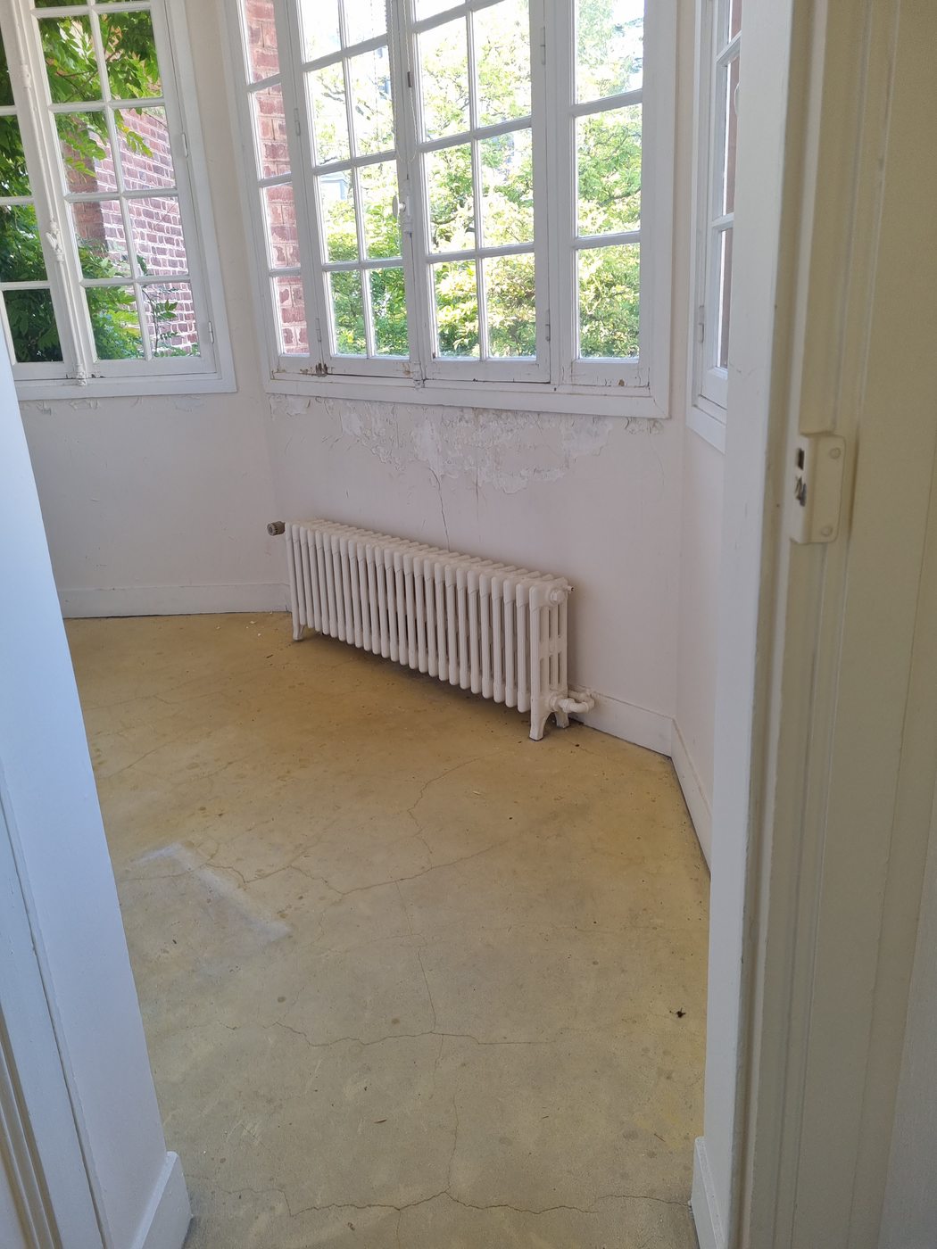 Radiateur fonte à colonnes basses posé sous une baie vitrée dans une maison ancienne