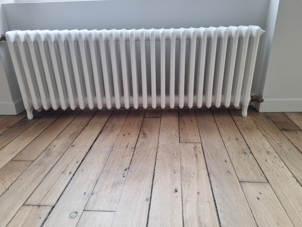 Radiateur fonte à colonnes posé sous une fenêtre à garde-corps en fer forgé
