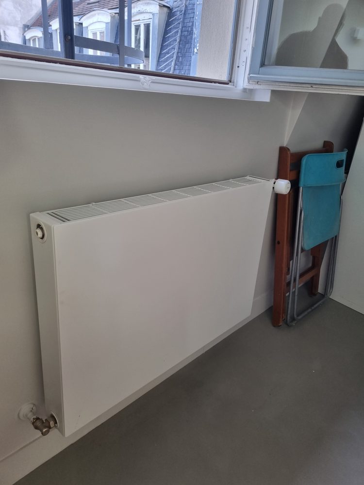 Radiateur panneau acier remplacé sous une fenêtre dans un appartement parisien