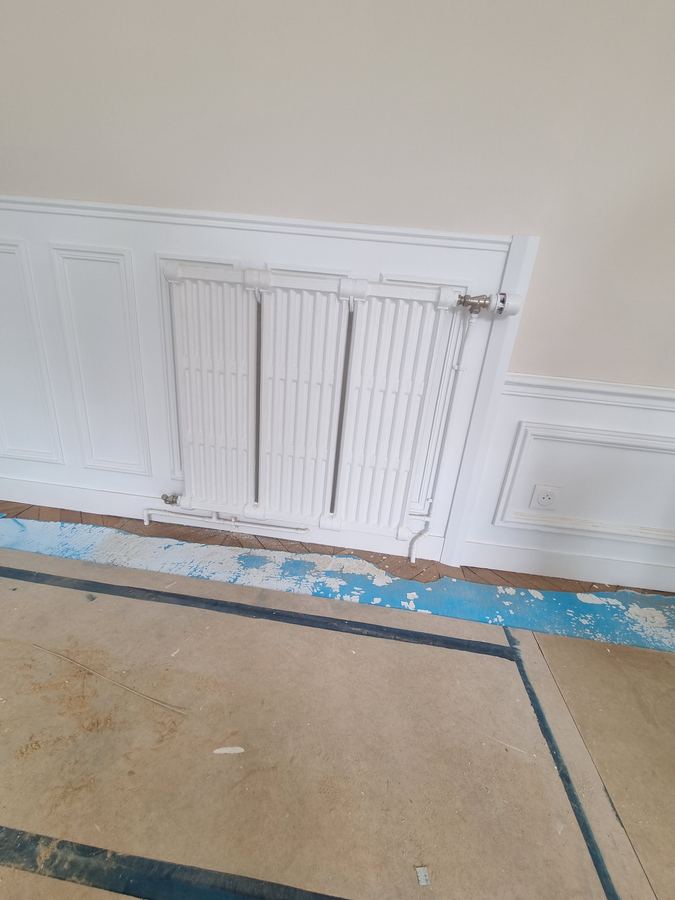Radiateur fonte à colonnes reposé dans une boiserie haussmannienne, robinet thermostatique neuf