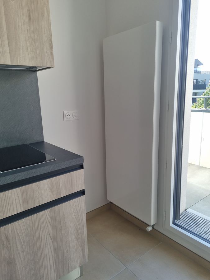 Radiateur vertical acier posé dans une cuisine en angle de baie vitrée