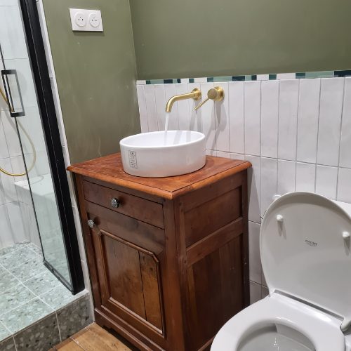 Vasque à poser sur meuble ancien en bois à côté d’un WC