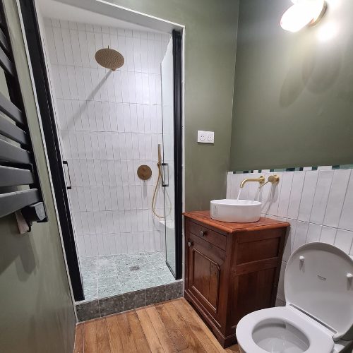 Douche à paroi noire, WC et sèche-serviettes dans une salle de bain rénovée